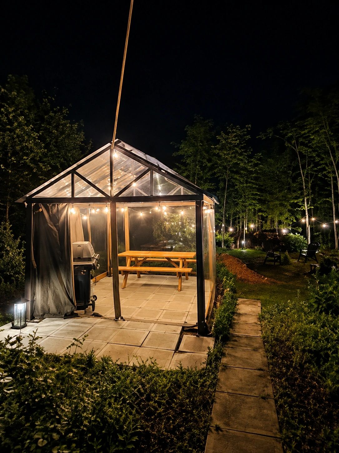 Glass gazebo lit up at night with picnic table and forest surroundings